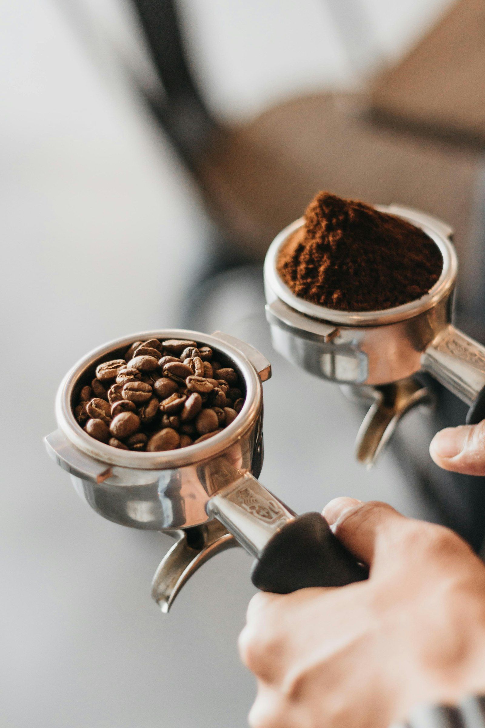 Barista holding two espresso portafilters with fresh ground coffee and whole beans